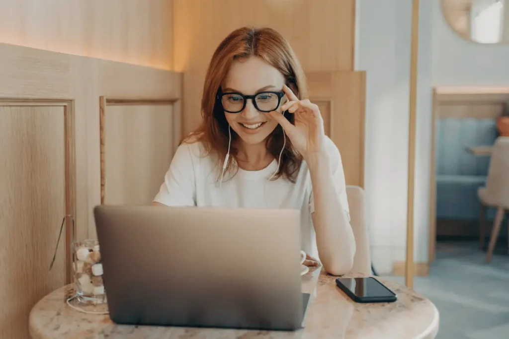 Key-features-of-optometry-websites_img-Blog a woman smiling and looking at her laptop in a cafe